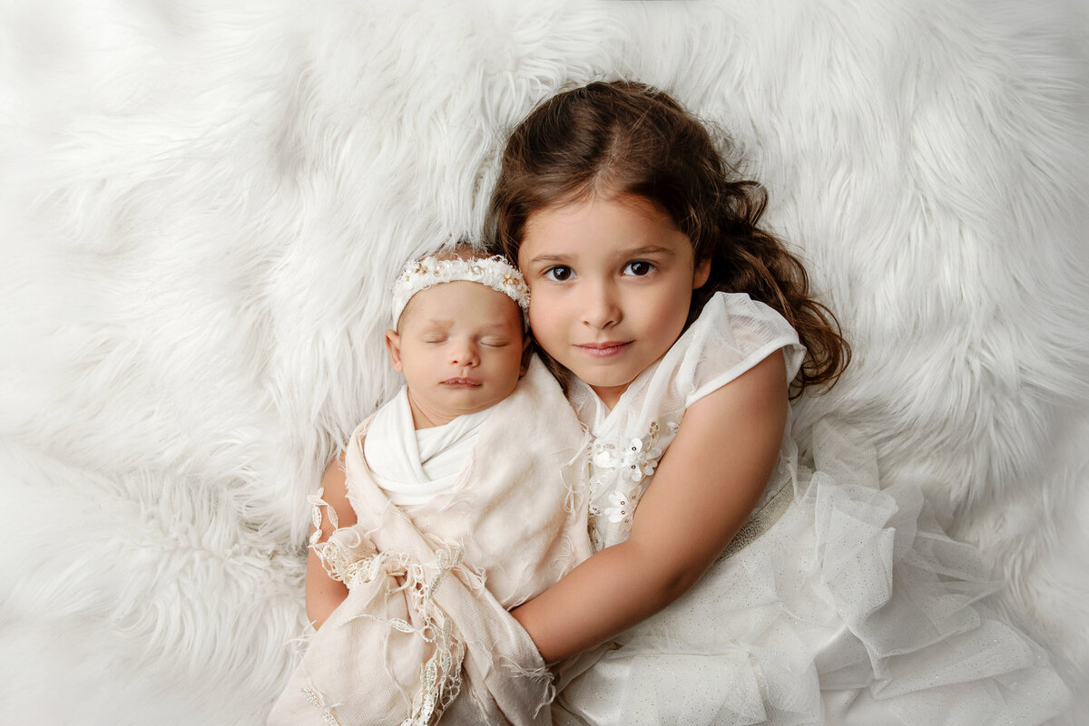 st-louis-newborn-photographer-big-sister-holding-newborn-girl-on-white-fur