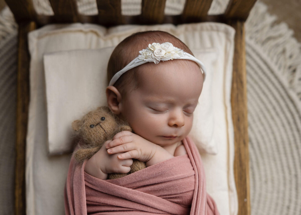 close up of newborn baby asleep holding a tiny teddy bear