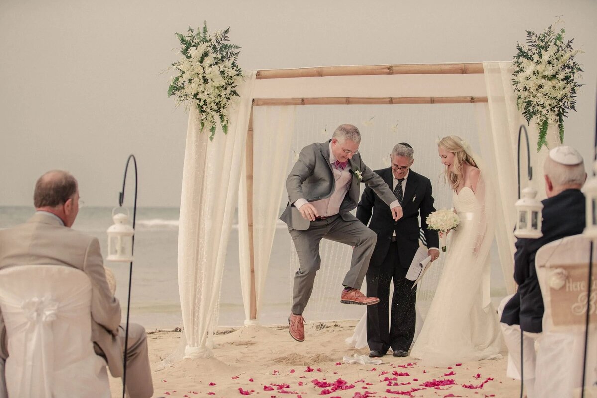 A groom leaps during a beach wedding ceremony