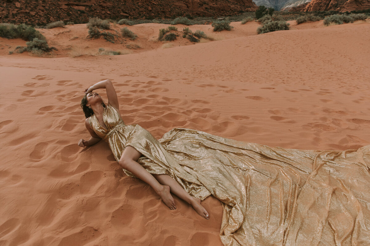 woman laying on the sand in gold gown