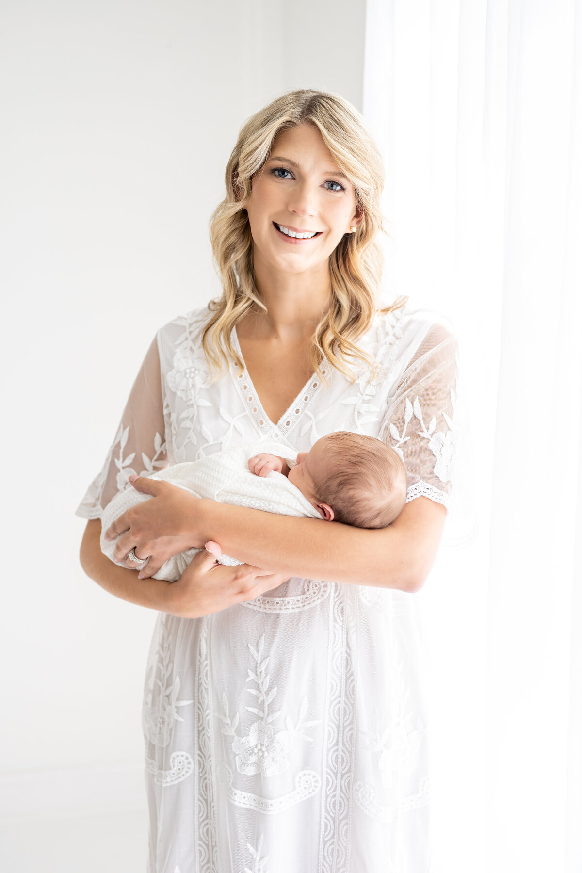 A new mother poses with her newborn by a window for newborn pictures