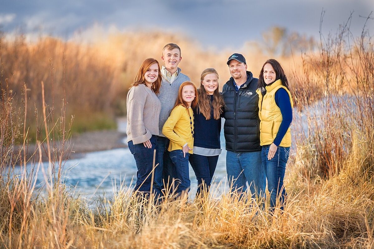 With hues of blue and yellow on a winter day next the Laramie river stands a family dressed warmly together on a cold winters day.