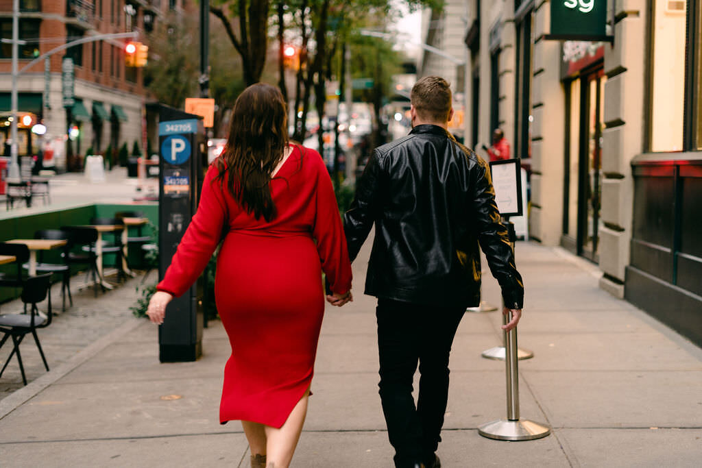 couple holding hands and walking down a sidewalk surrounded by stores and restaurants