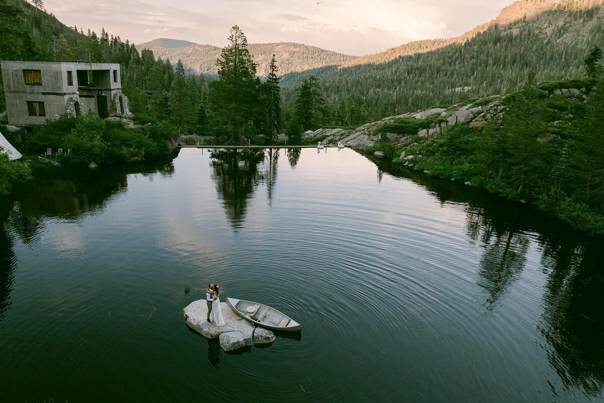 newlyweds on a rock in middle of small lake with canoe  over view of the whole scene at White Wolf in Alpine