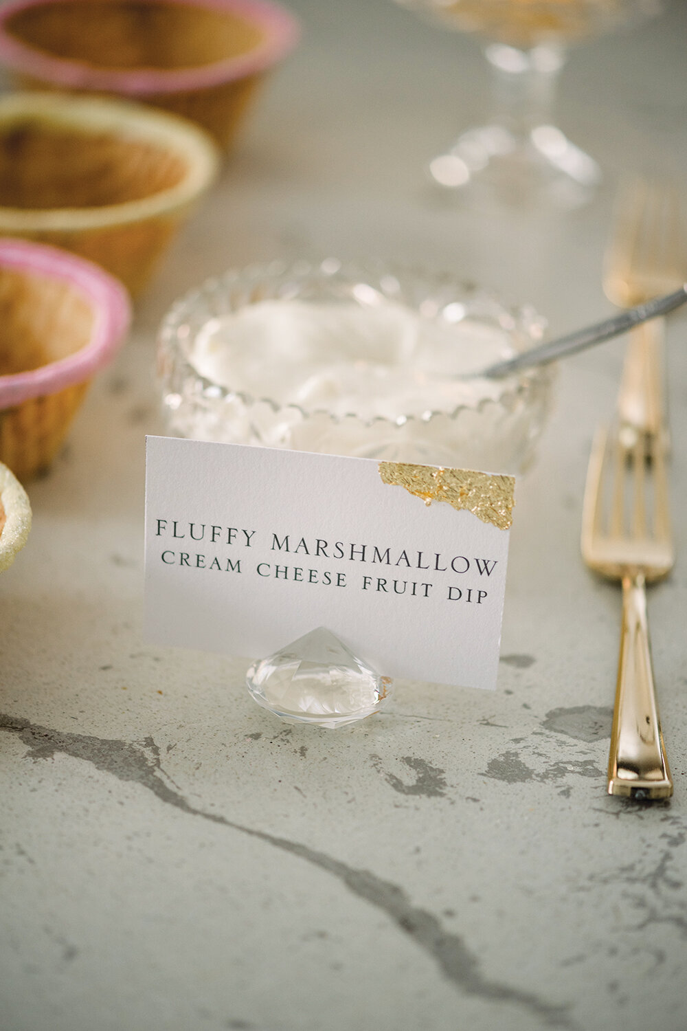 Elegant food label card with gold leaf detailing, displayed in a crystal holder, at a pink and yellow girl baby shower.