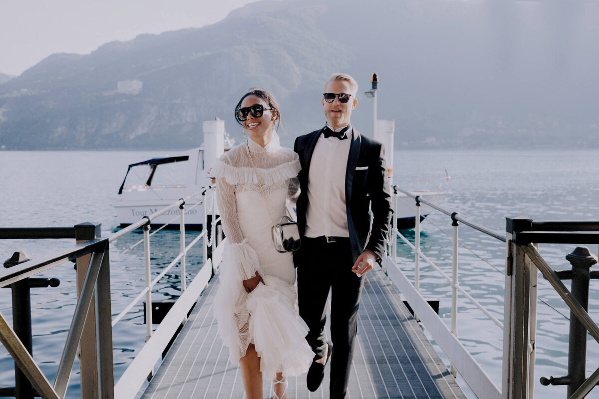 Bride and groom walking on a dock with a boat, ocean and mountain on the background