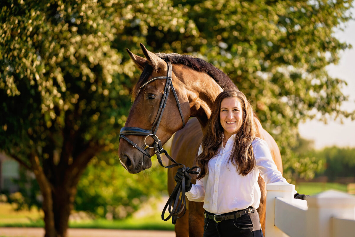 Dressage trainer poses next to a bay warmblood horse during a personal branding session.