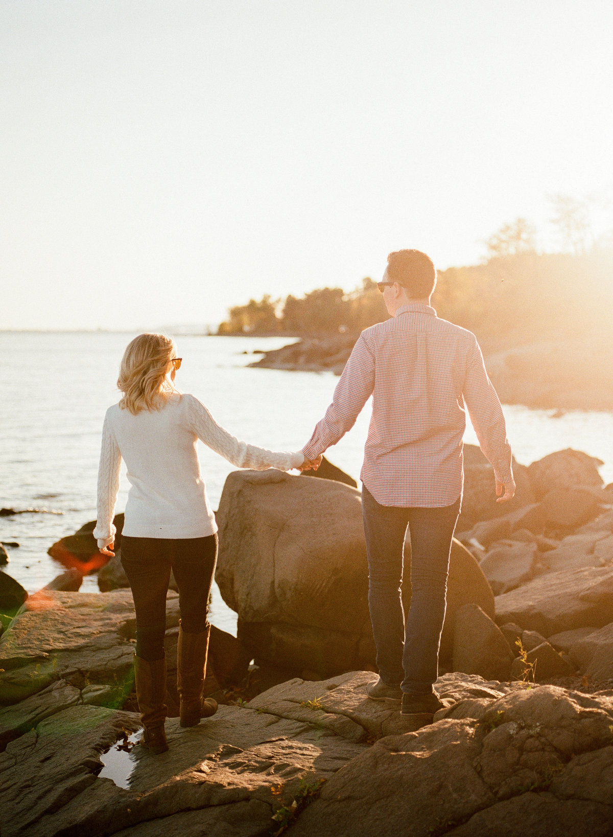 couple walks together over rocks of lake superior over sunset