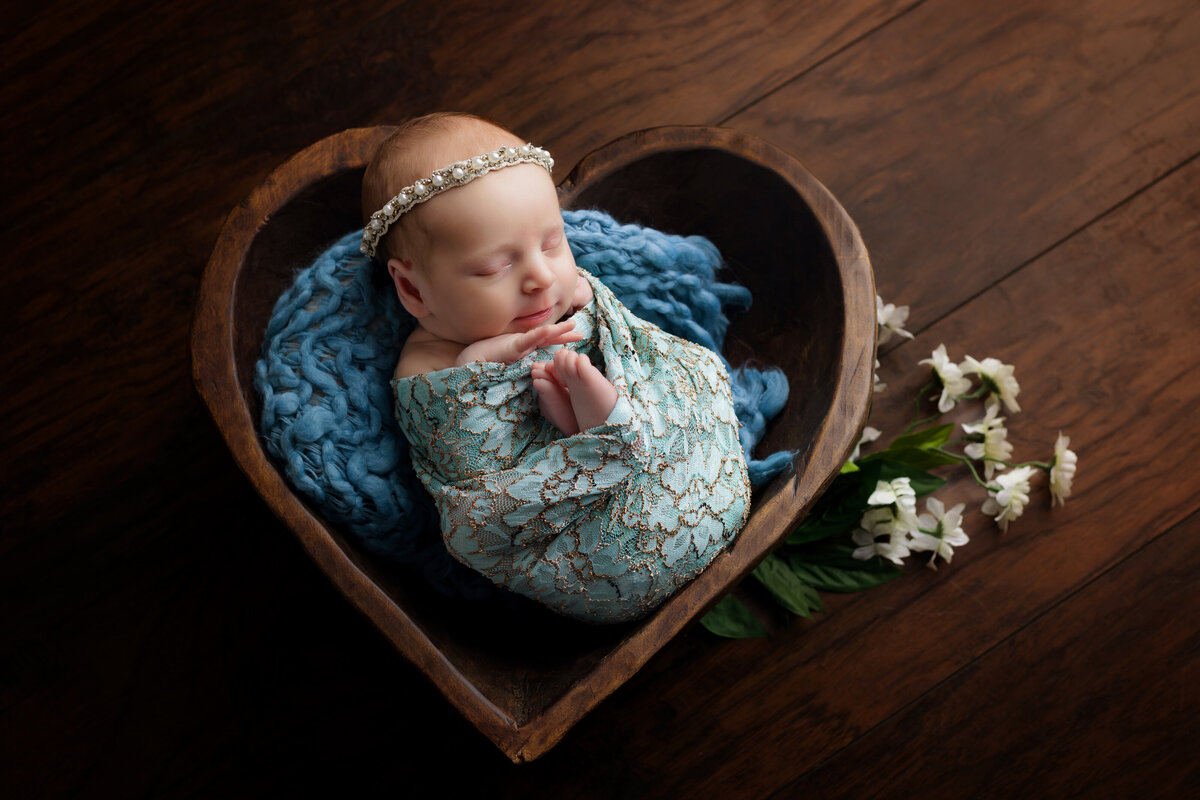 Newborn Photographer, a baby sleeps swaddled in a heart shaped basket