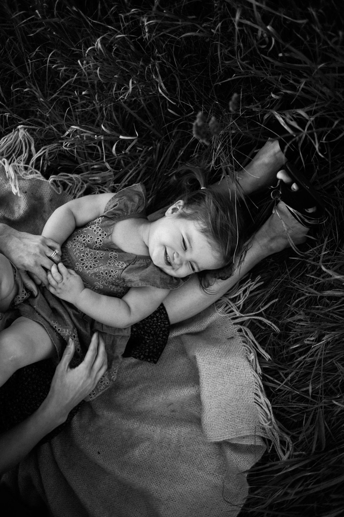 Mom tickling her baby girl on a blanket in an open field