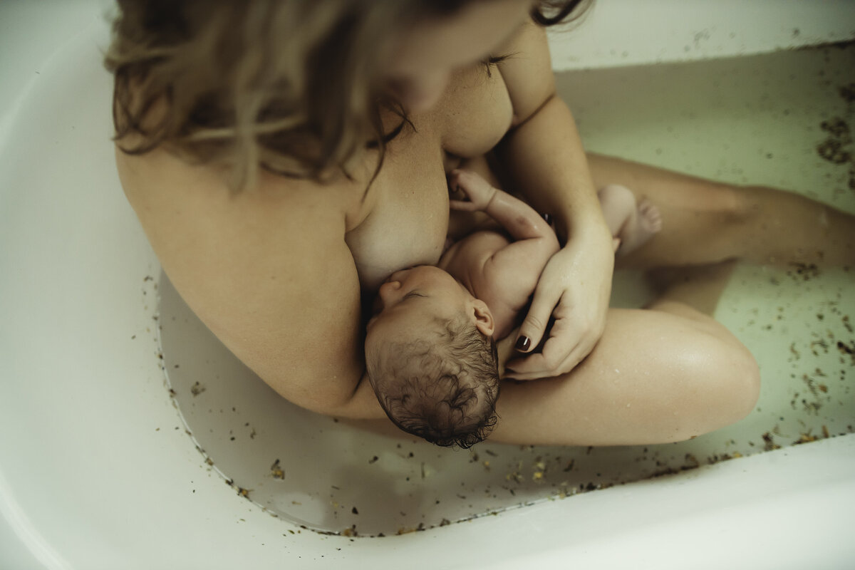 a mom cuddling her newborn baby at home in a herbal postpartum bath soak in pinellas county fl