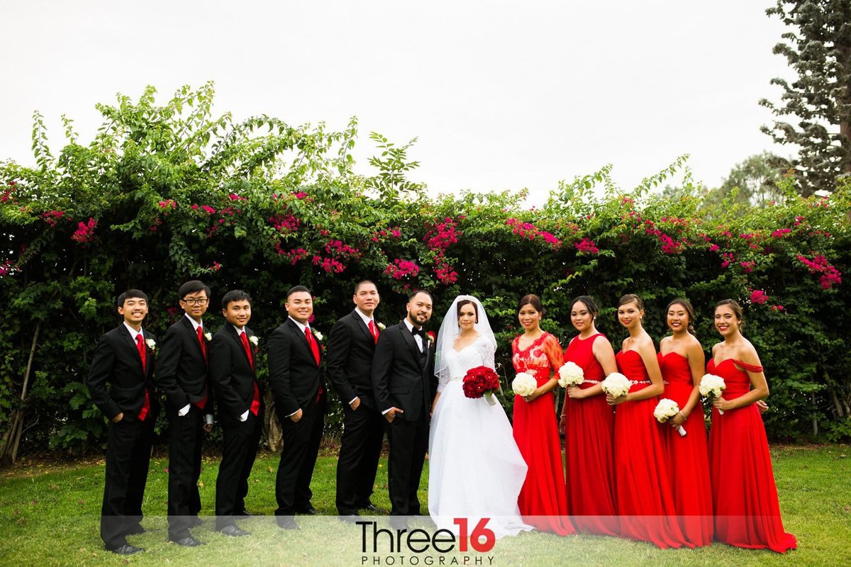 Bride and Groom pose with their wedding party all wearing black and red