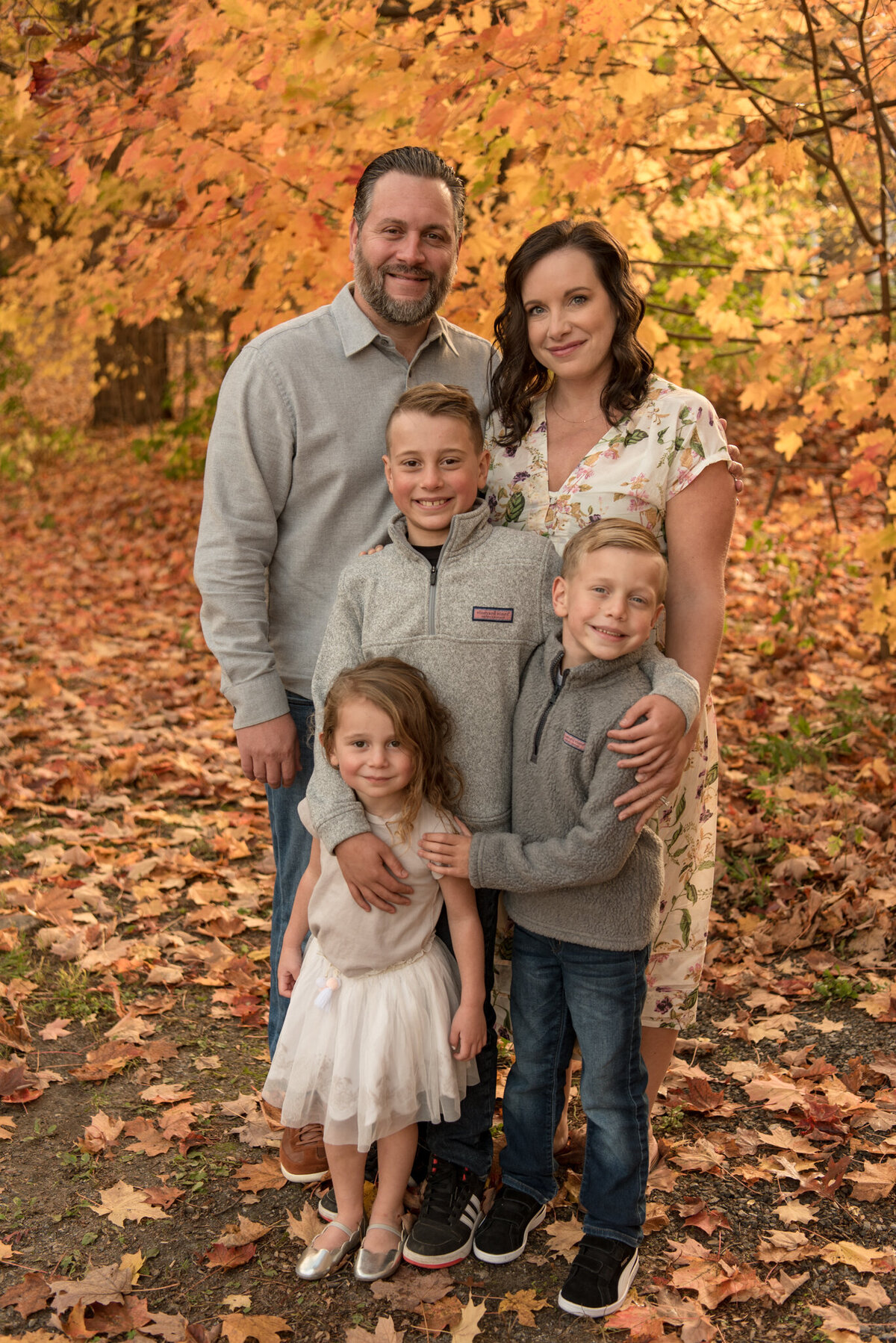 Family of five smiling at the camera with orange leaves behind them