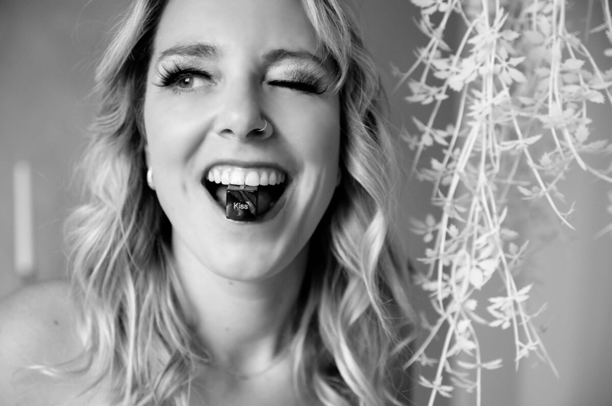 black and white photo of a woman with a dice in her mouth that says kiss while she is winking for her Mississauga Boudoir Photography session