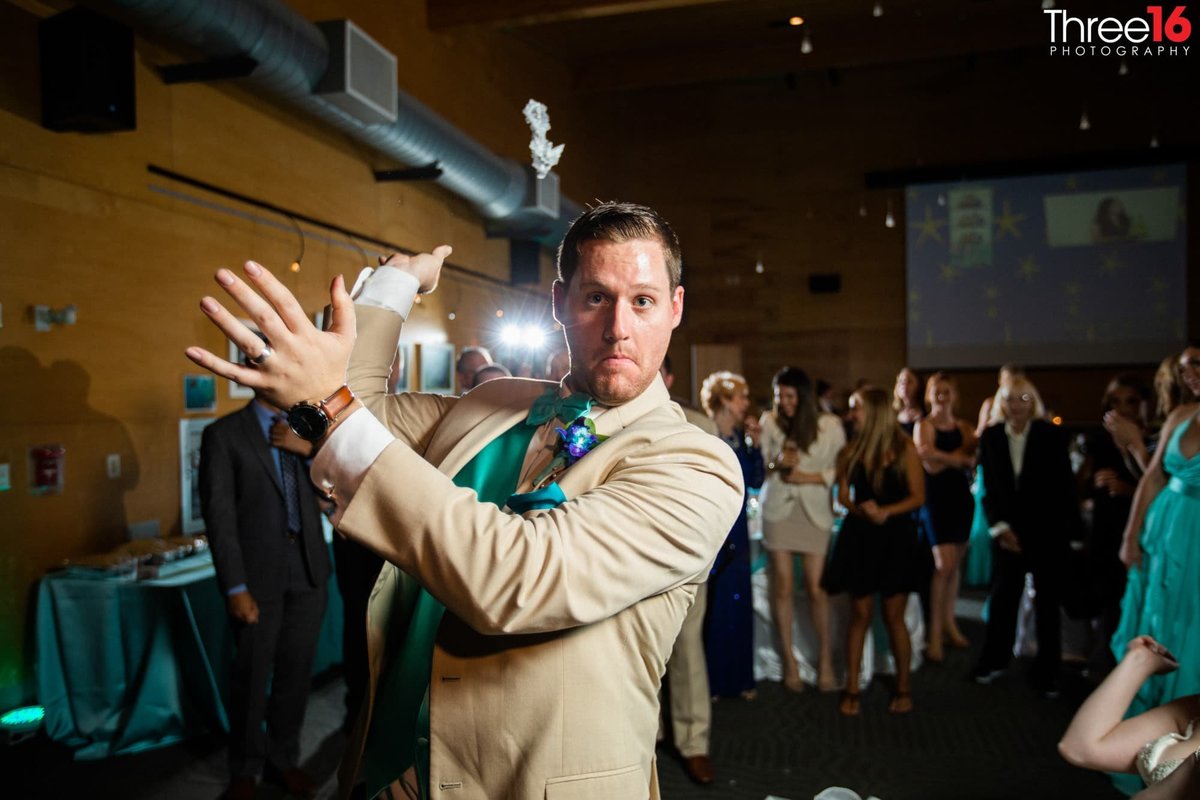 Groom stares at the camera as he flings the garter belt in the air