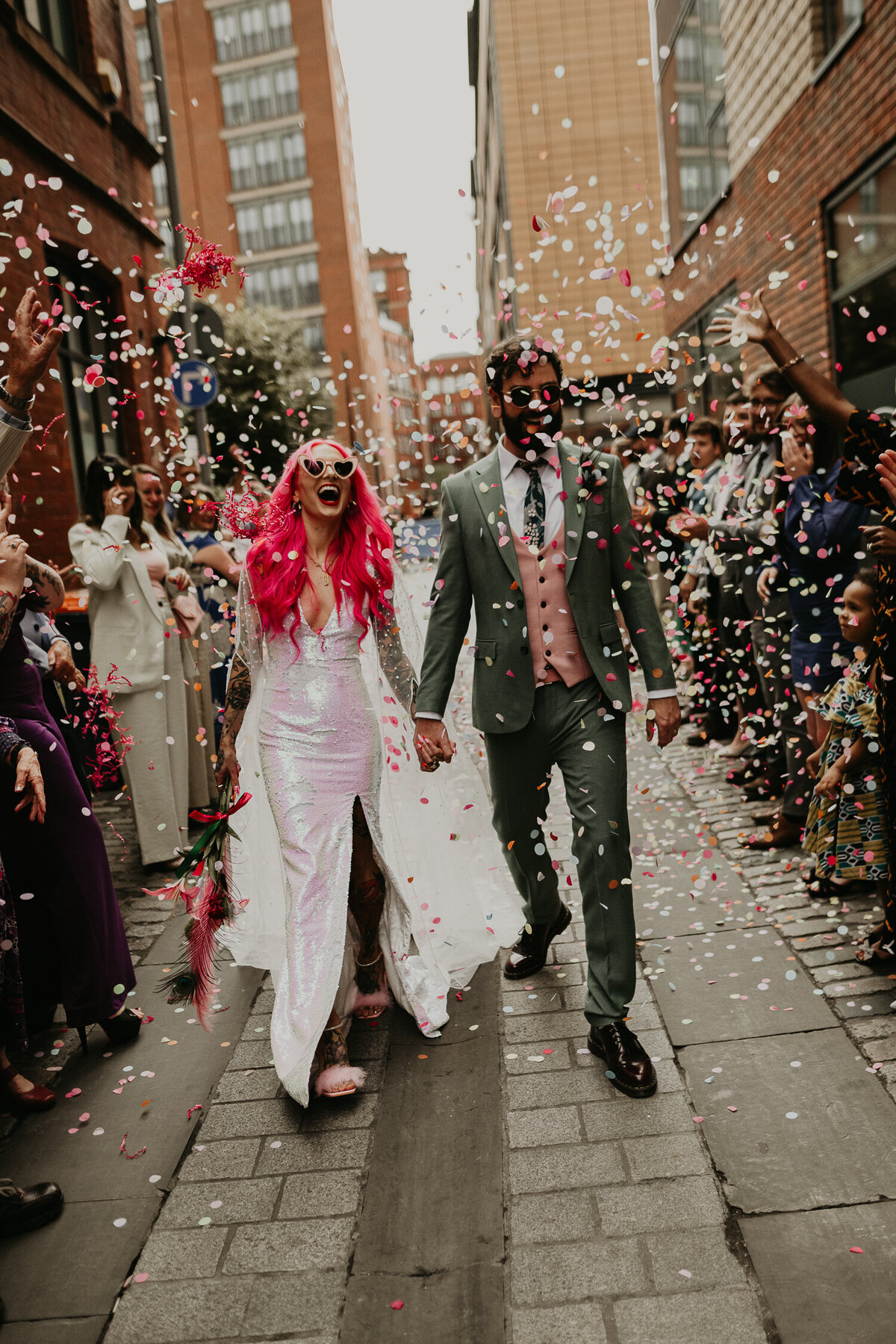 Tattooed wedding couple walk through a confetti line at their Manchester wedding venue.