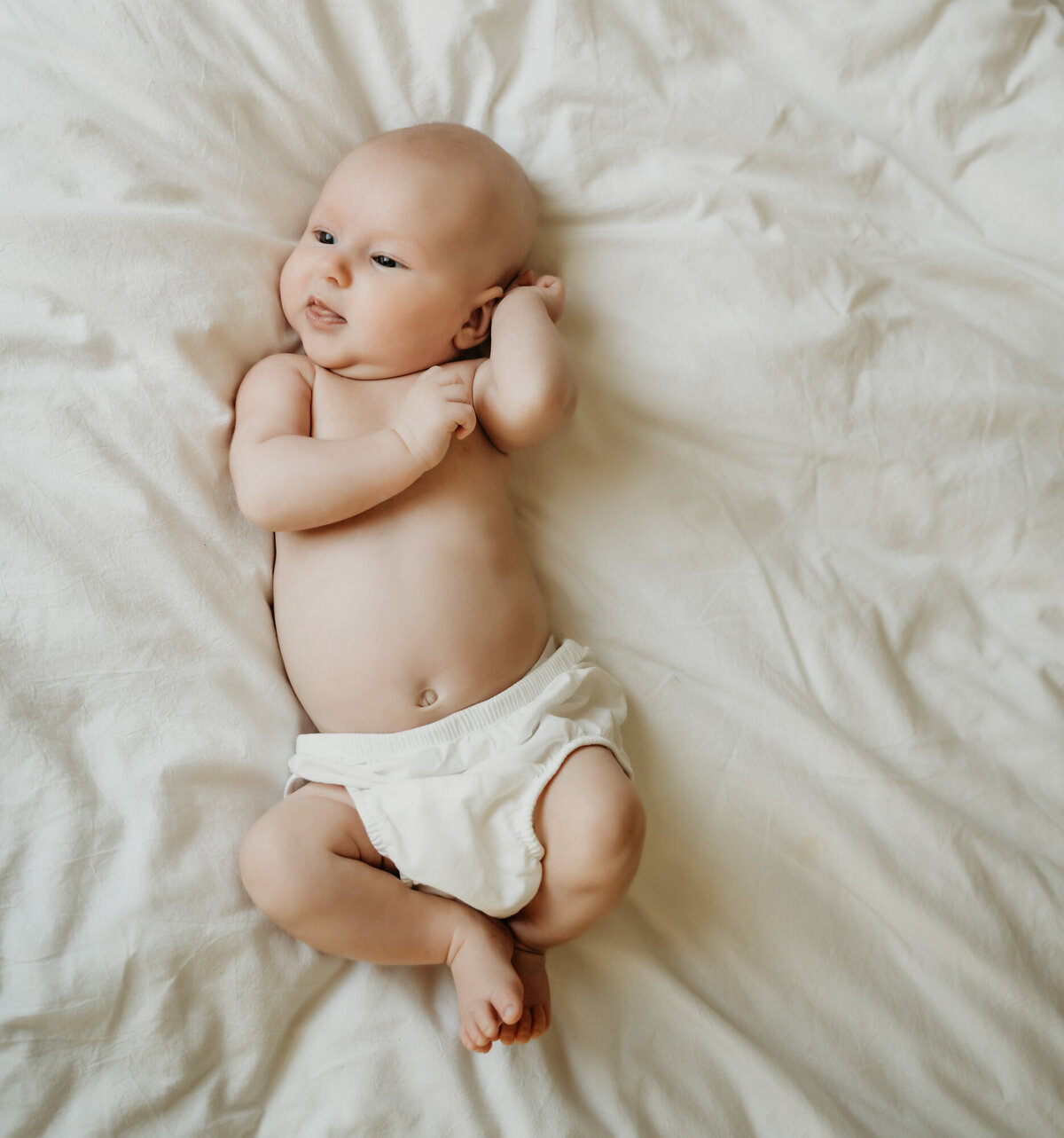 Newborn Photographer, Baby in a diaper cover on a white bed, stretching.