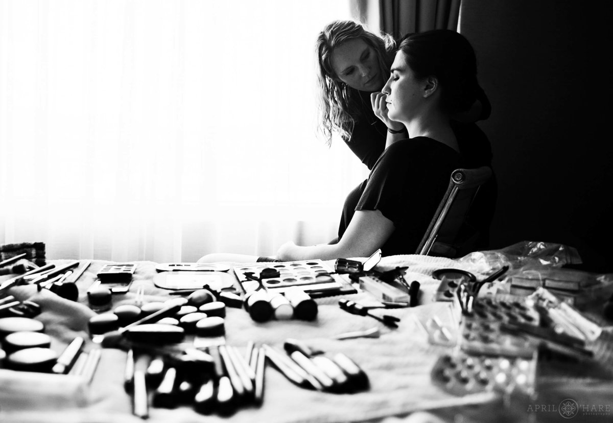 Make up scattered across hotel room bed as bride gets her make up done in a B&W photo in Boulder Colorado