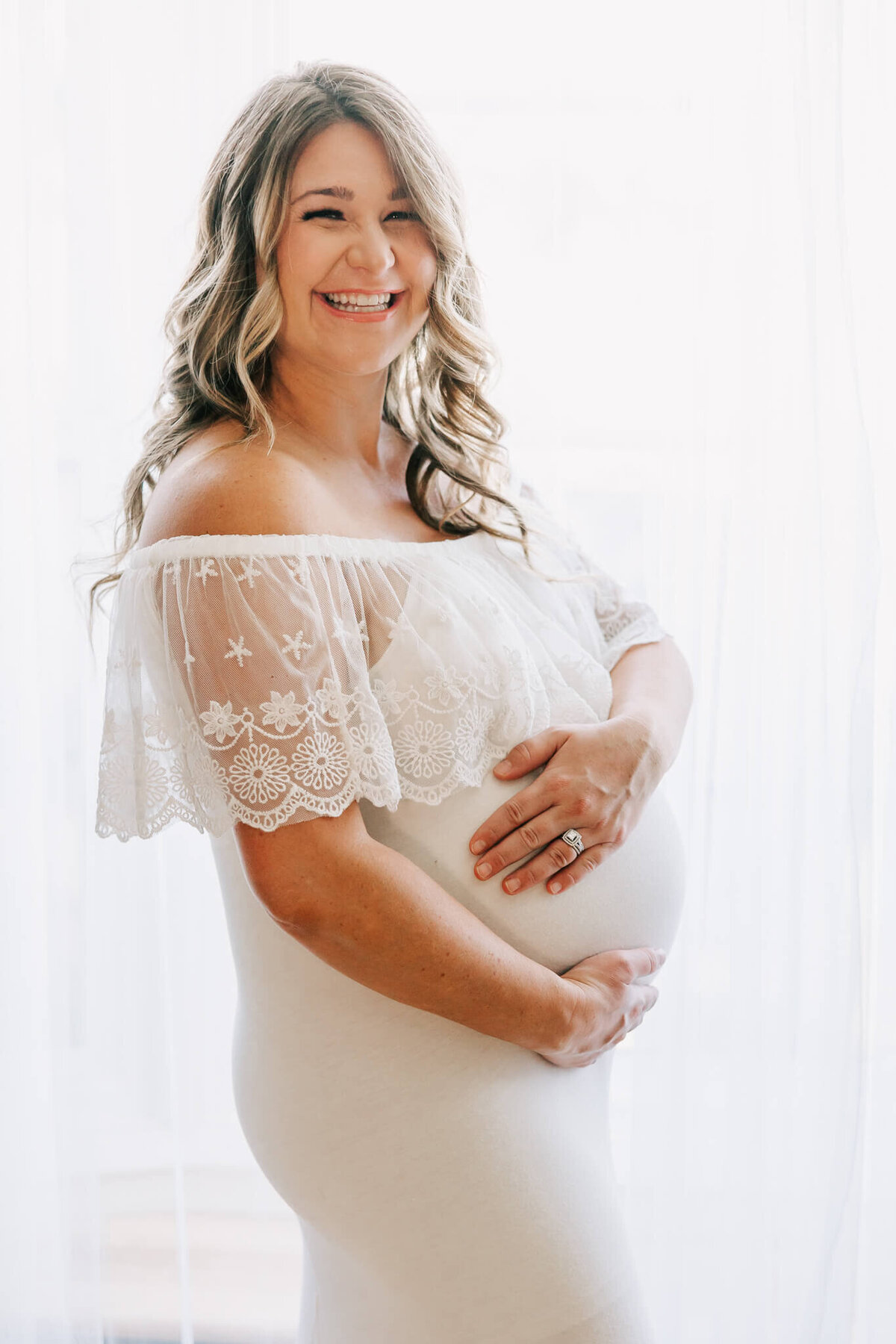 gorgeous backlit happy maternity portrait of a woman in a white dress