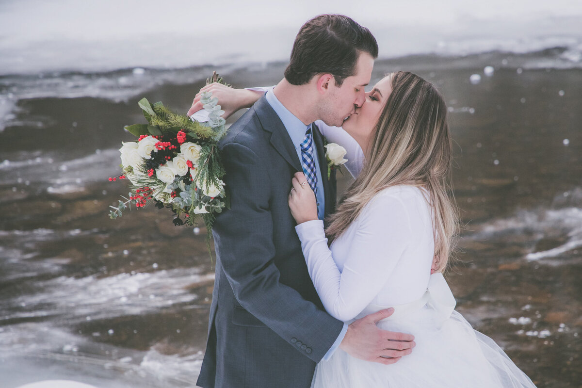 Bride and groom kiss with frozen lake behind them.