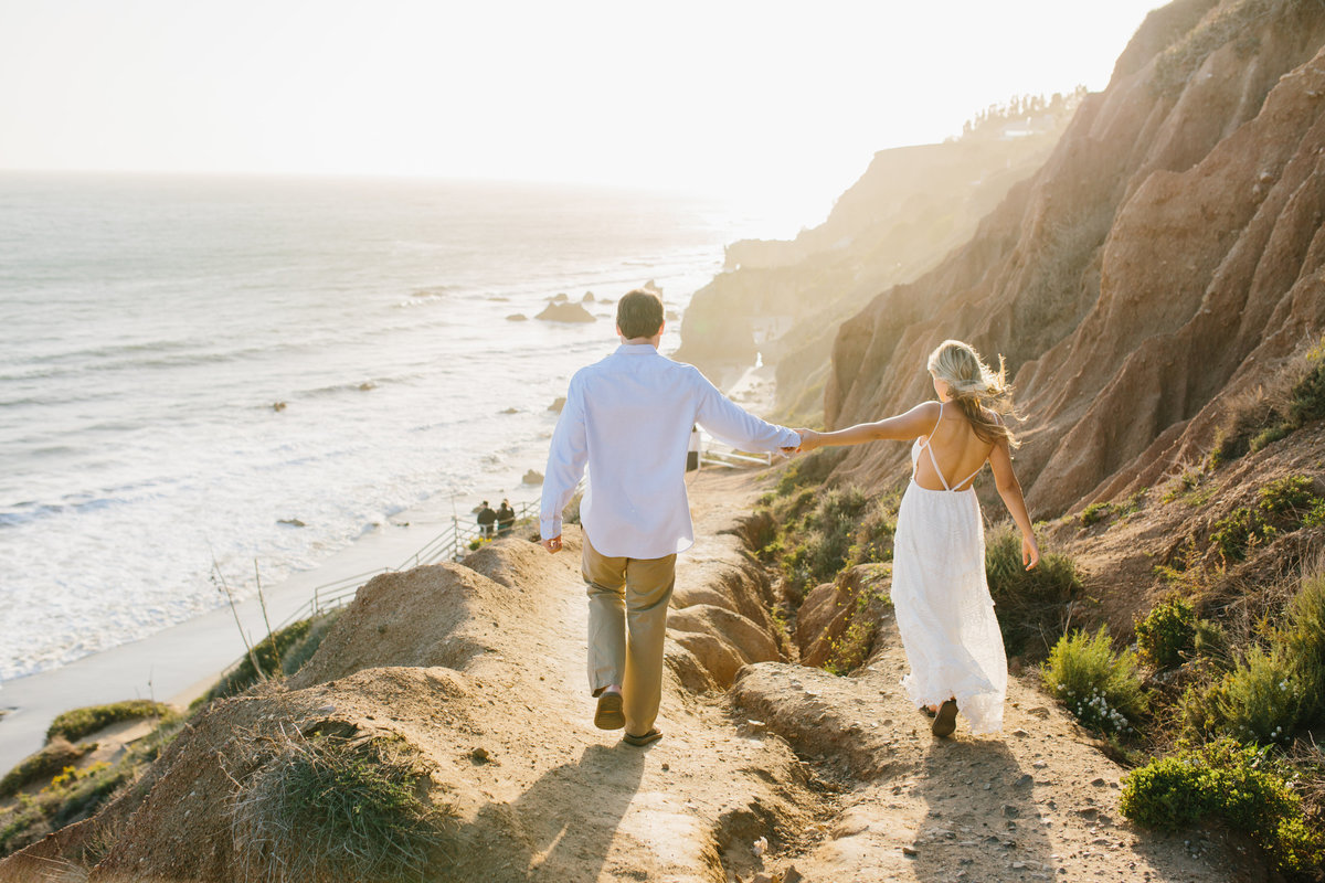 Couple walking down a path holding hands to the beach in Malibu California
