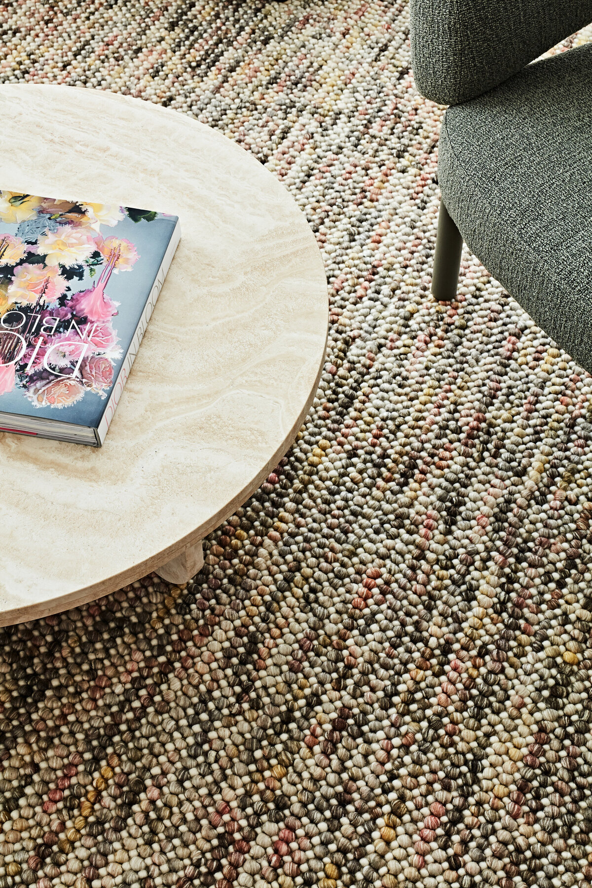 Close-up of textured coffee table and boucle rug with Dior book and soft lighting