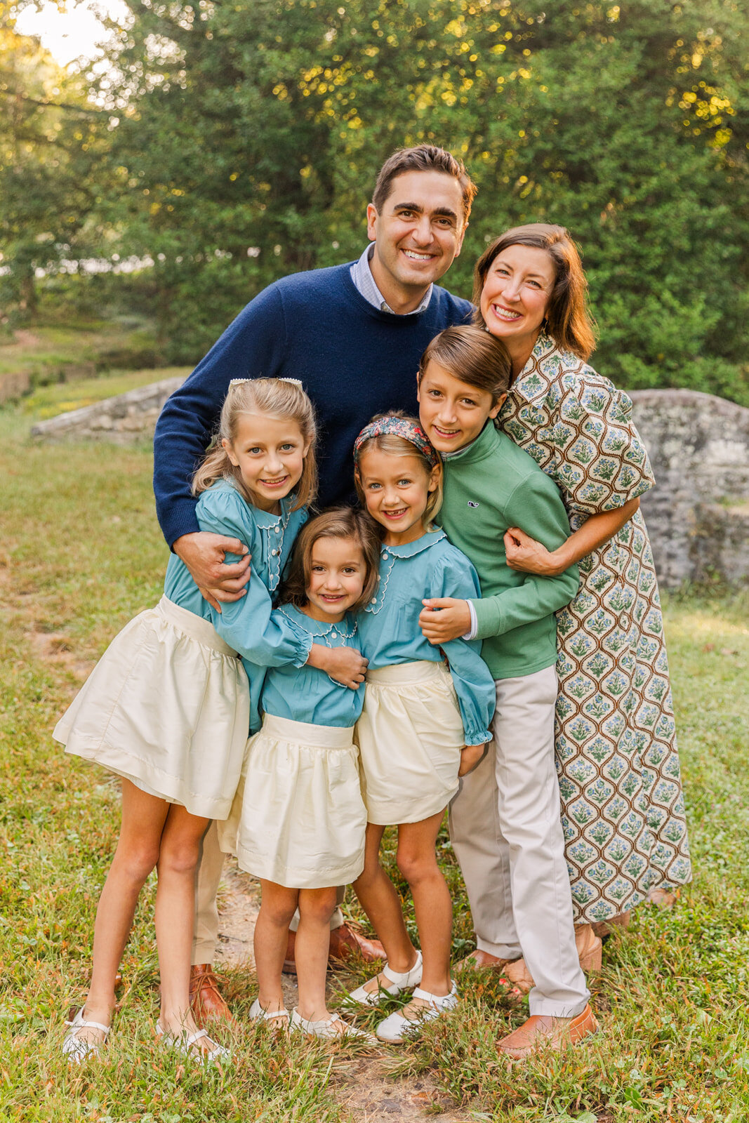 Family hug during photo session in an Atlanta park, 3 sisters wearing matching white skirt and blue top all wearing coordinated blue and green outfits by Laure Photography