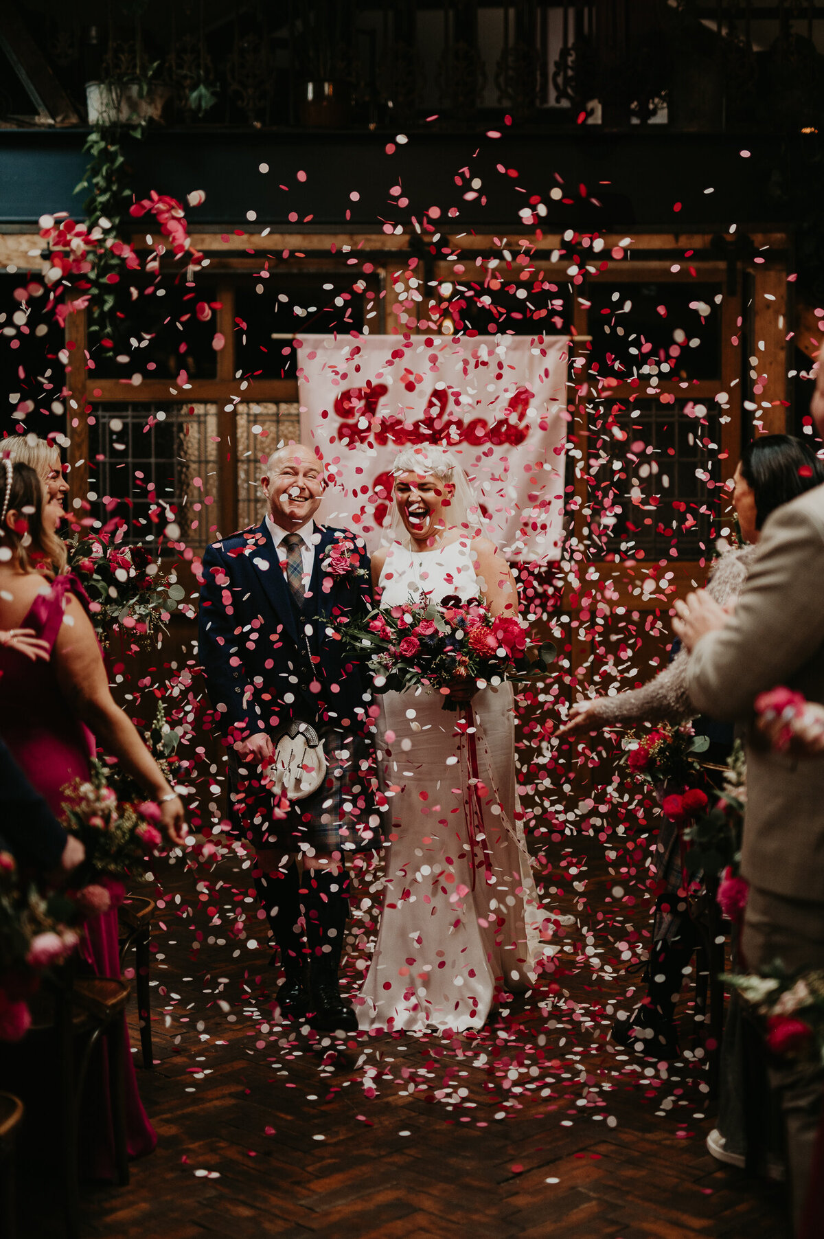 A bride and groom walk up the aisle whilst being covered in confetti at Clapton Country Club.
