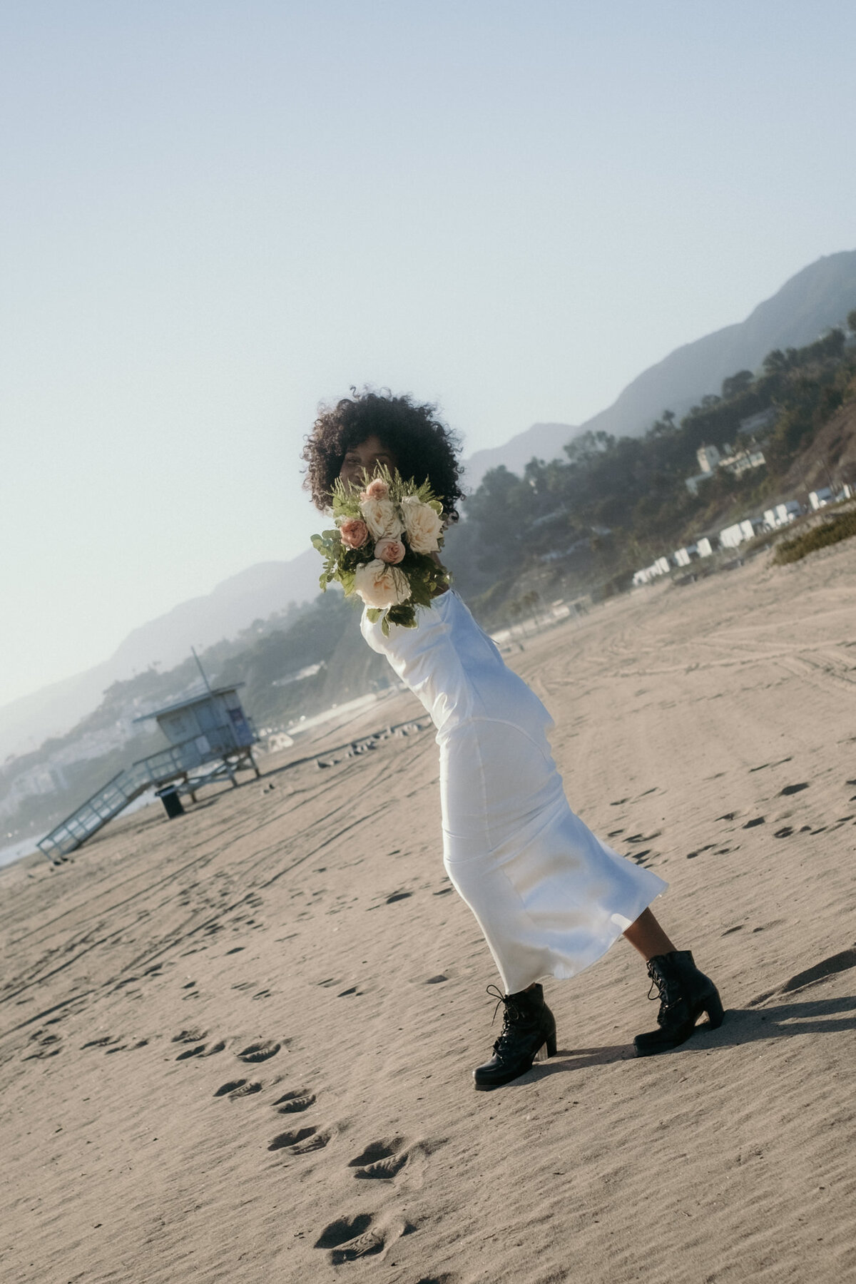 Den Strauß vor ihrem Gesicht präsentierend läuft die Braut über den Sand.
