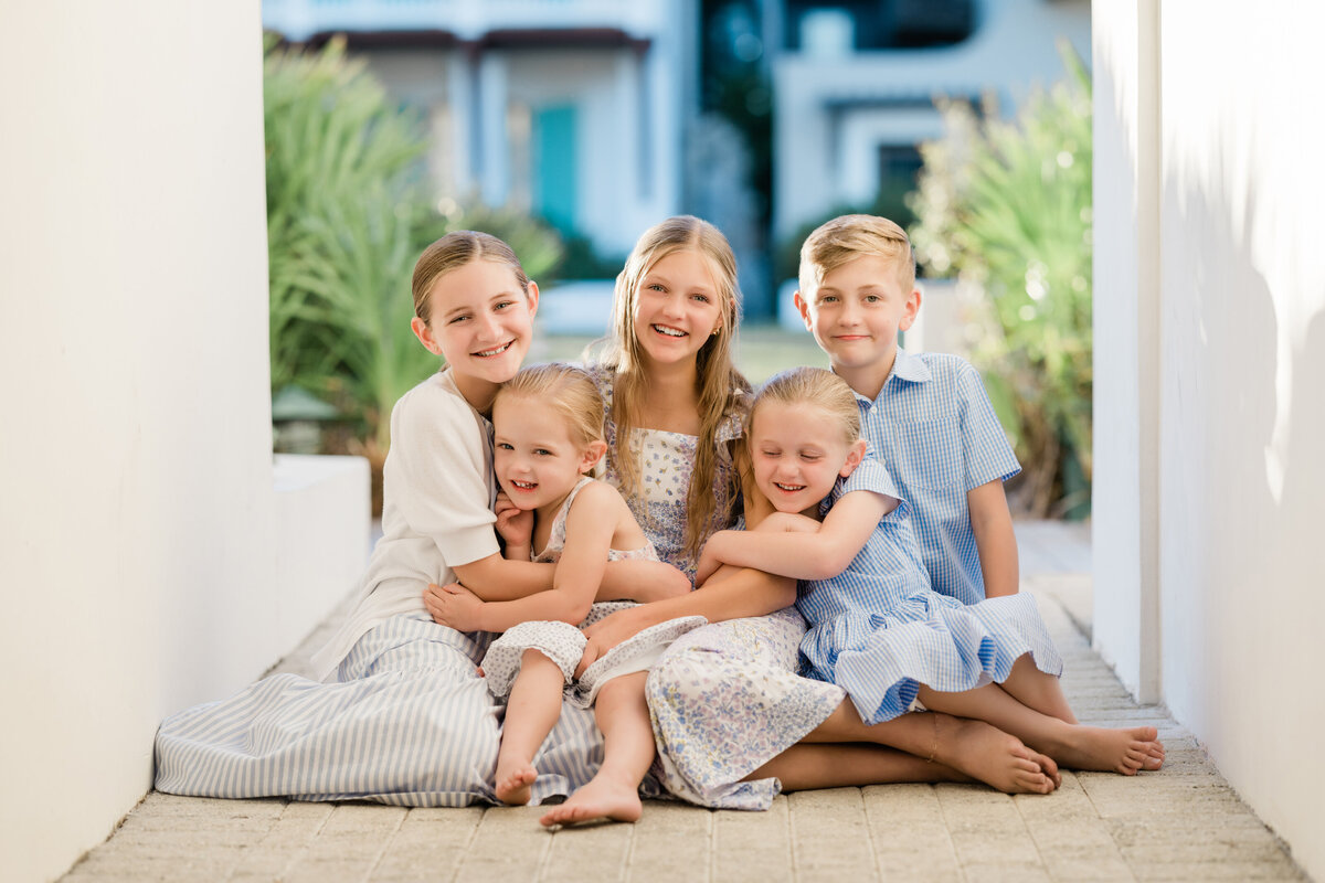 Five siblings sitting on the ground together smiling near Eastern Green in Rosemary Beach.