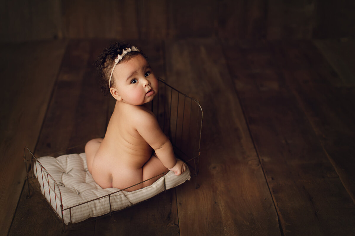 baby girl on bed on wooden backdrop