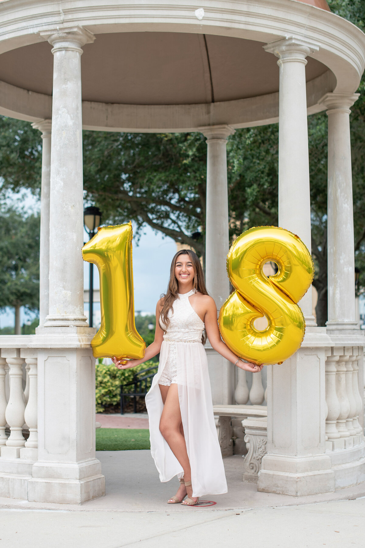 High school senior girl holding gold "18" balloons.