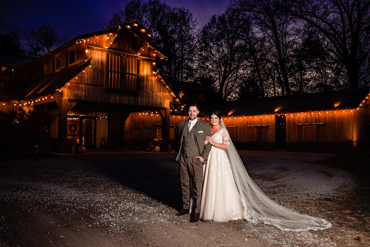 Bride and groom standing outside Copper Ridge Wedding venue at sunset with lights lit behind them