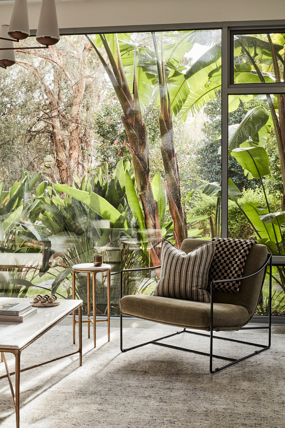 Melbourne interior design project featuring modern armchair and side table in glass-walled living space overlooking tropical garden.