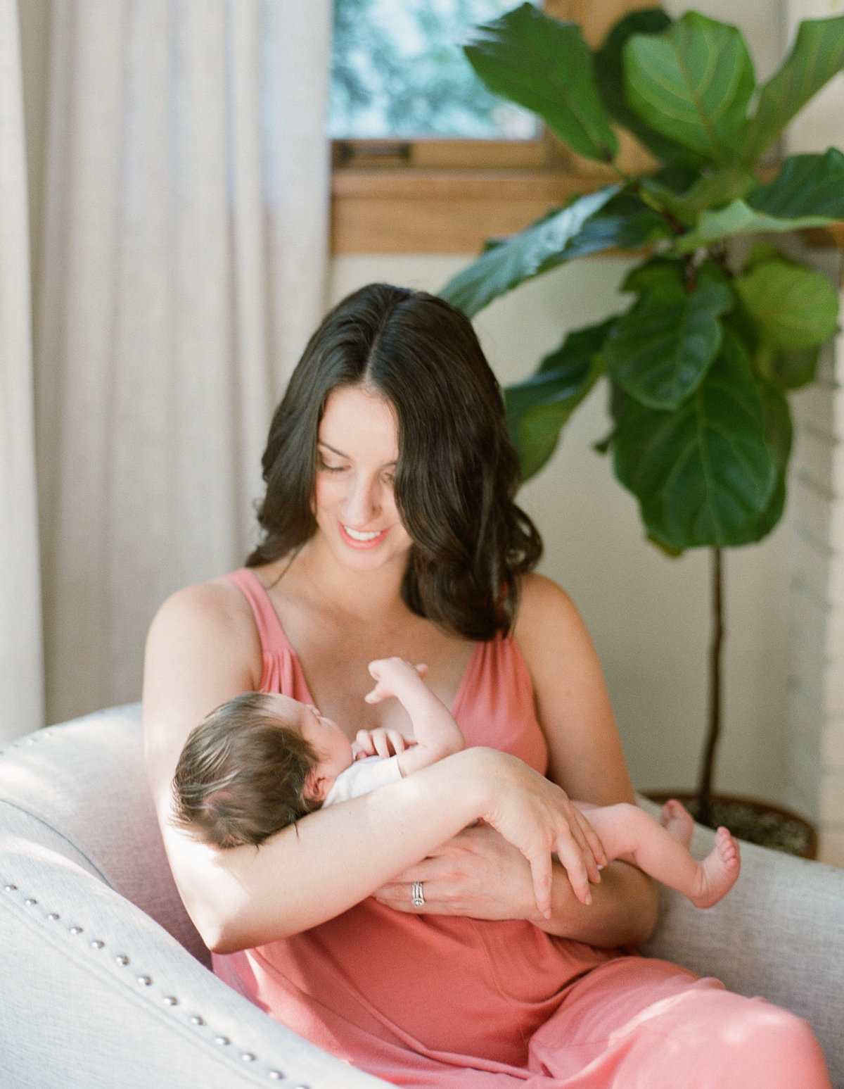 mom holds newborn baby in living room chair with fig tree in the background