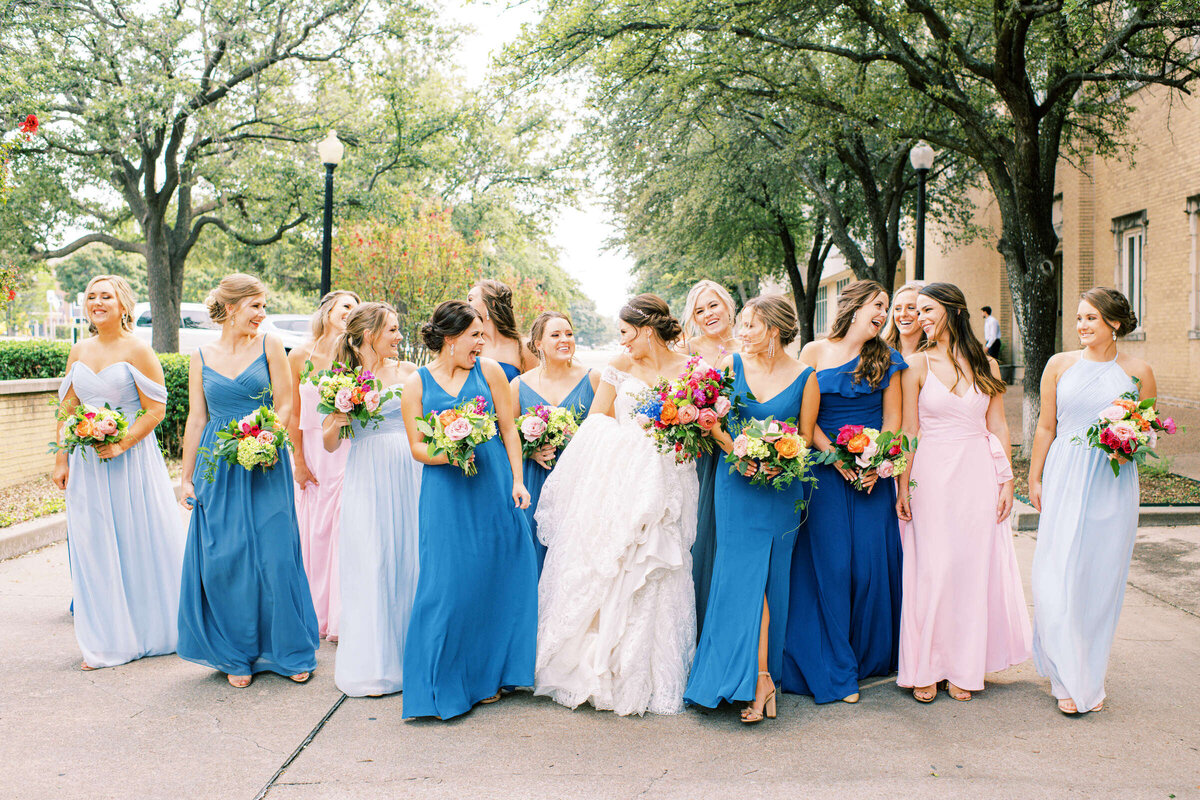 Bride and colorful bridesmaids walk and smile together at summer wedding in Fort Worth Texas