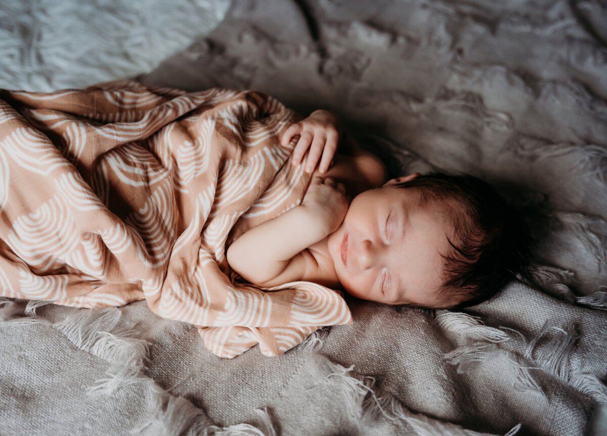 Newborn Photographer, a baby is swaddled in a blanket and sleeping on bed linens