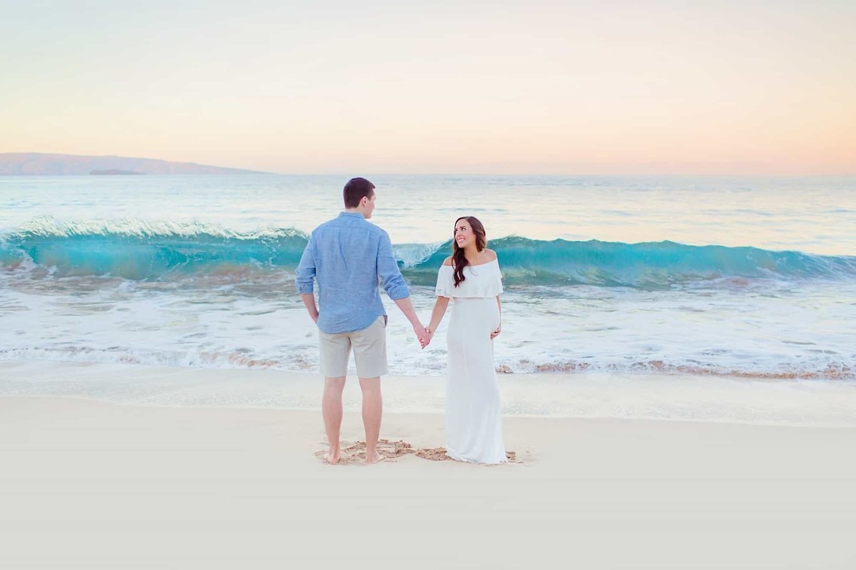 Couple holds hands and smiles on the beach in Wailea for their Love + Water maternity session