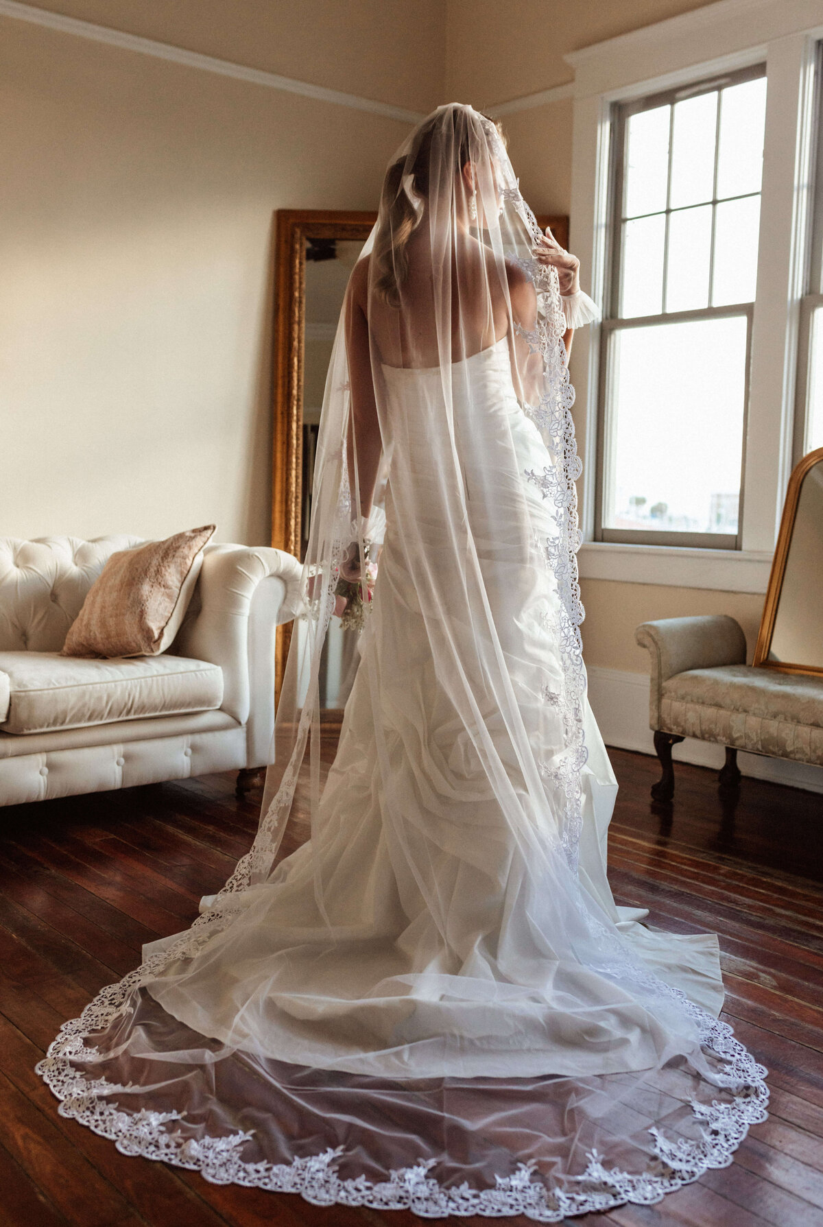 Bride looks into mirror, photo from back with veil draping her-in downtown Panama City wedding venue Sapp House