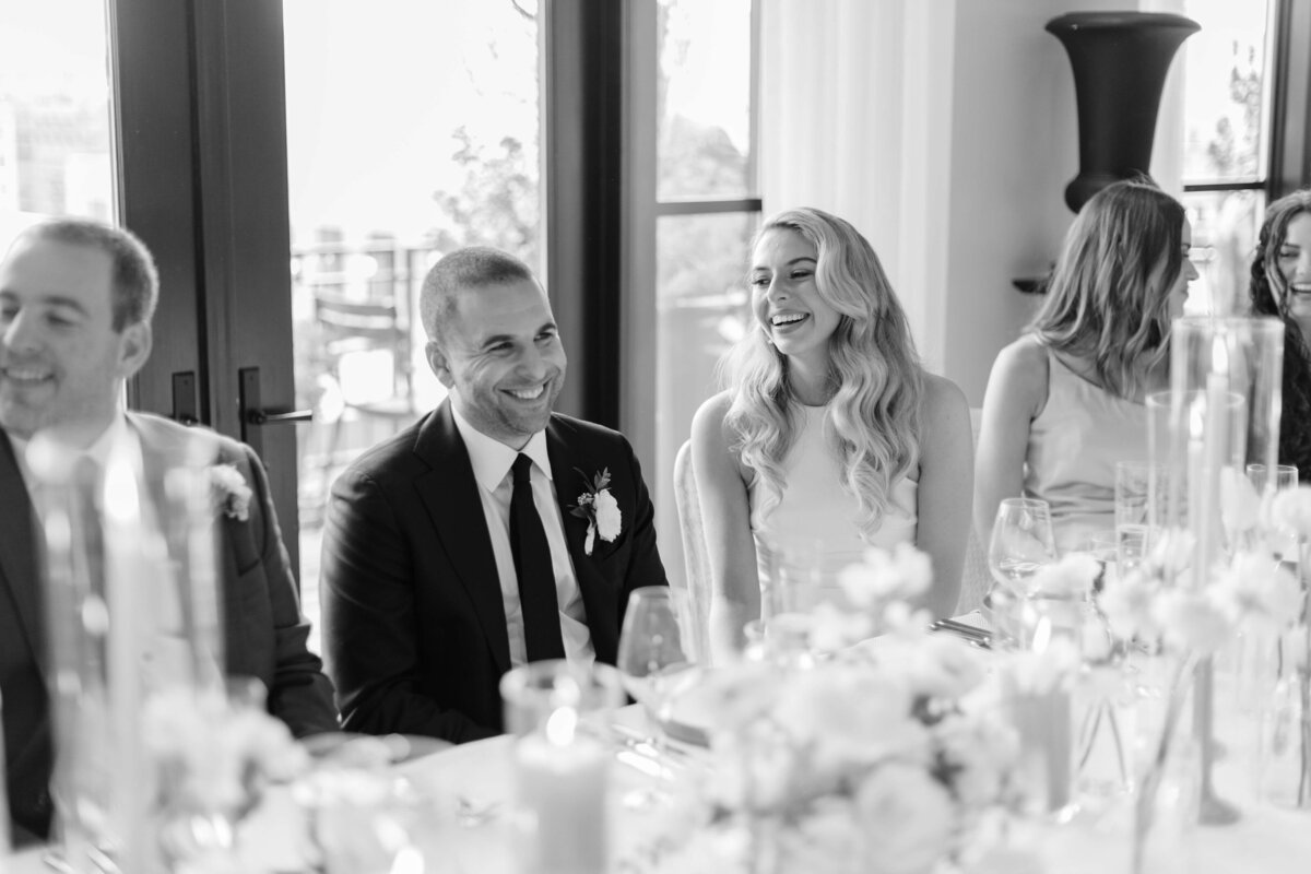 A bride and groom sit at a table laughing.