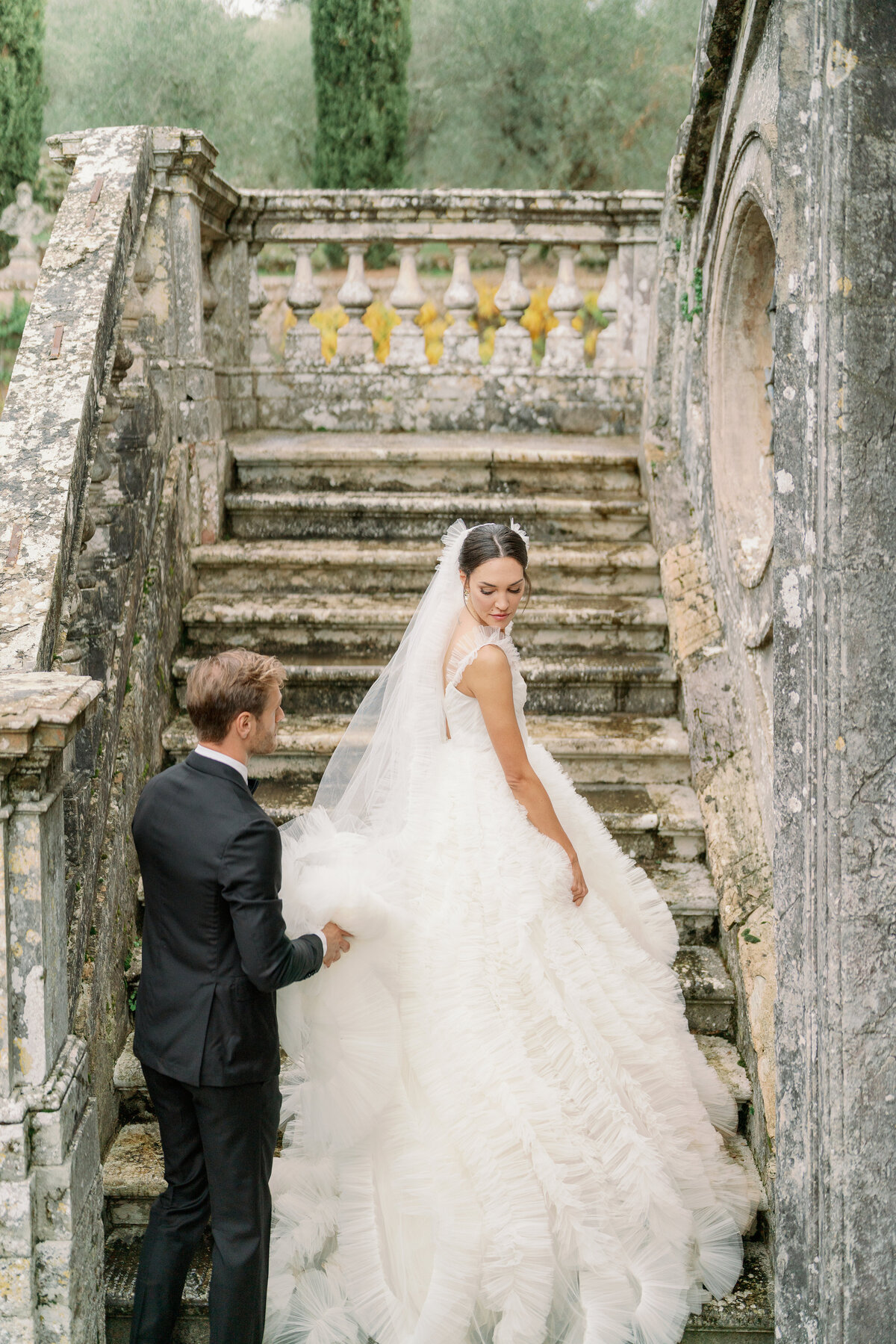 bride going up steps looking back at her groom holding her dress at a villa in Tuscany Italy
