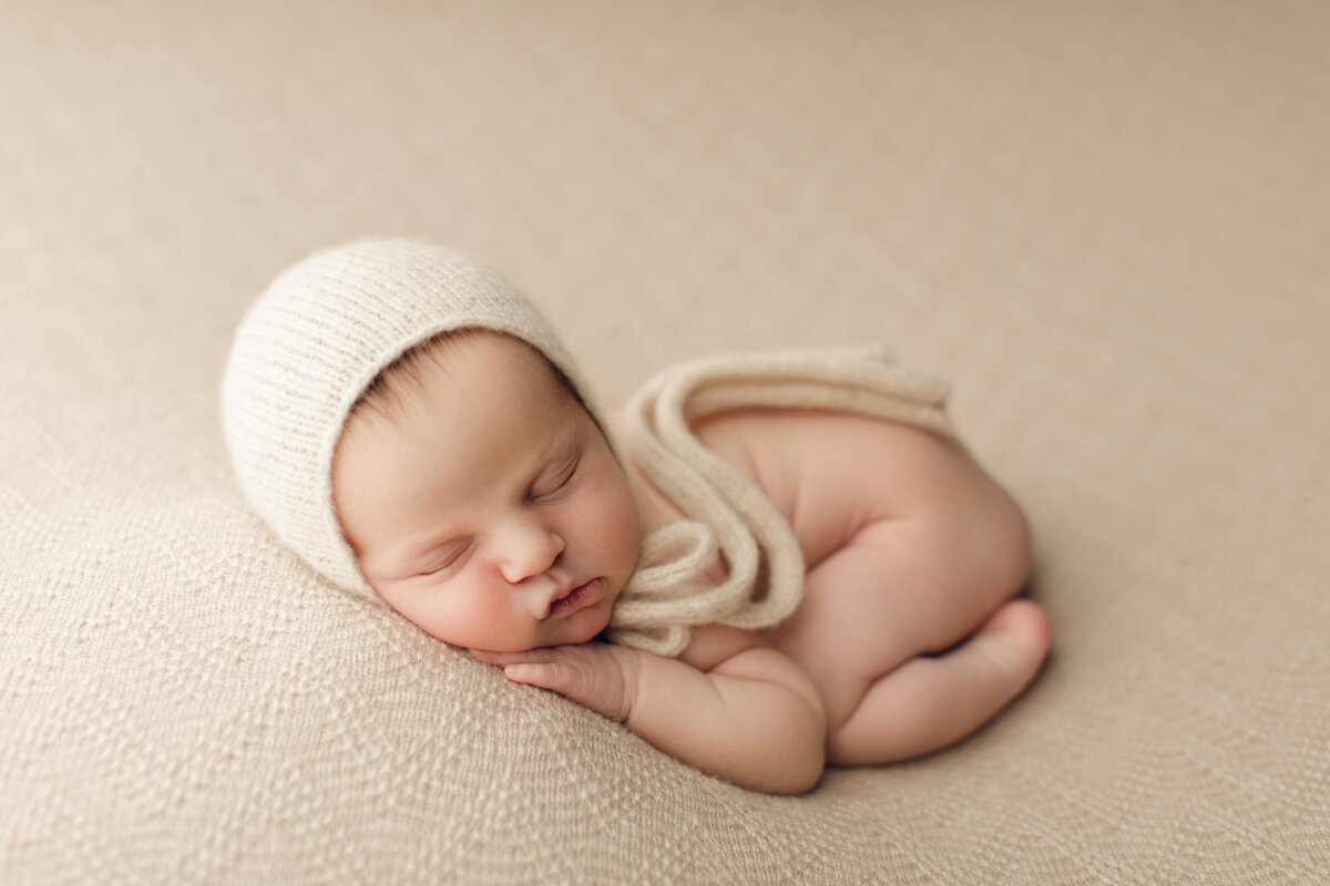 sleepy baby on neutral backdrop with cream bonnet