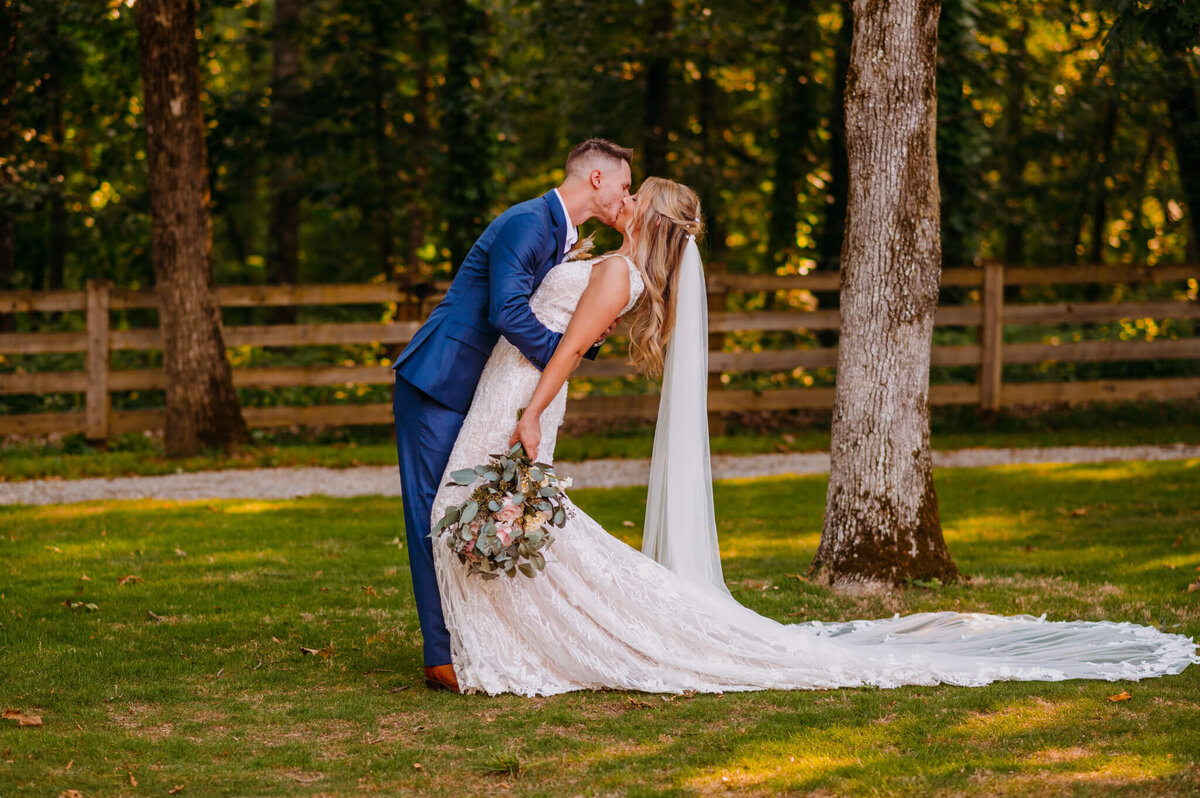 photo Of a bride and groom kissing on a lawn with trees and a fence in the background