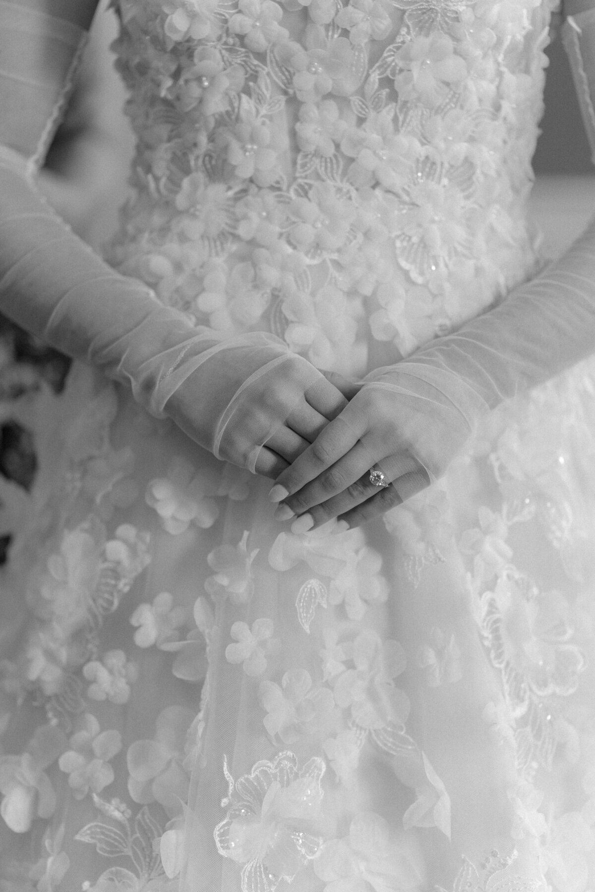Bride wearing sheer sleeves that partially covers hands. Bride holding finger tips to show wedding rings. Flower embellished wedding gown. Black and white Charleston wedding photographer.