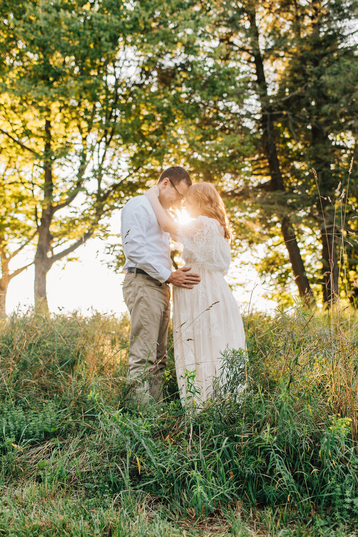 Expecting mom and dad embracing in tall grass at sunset