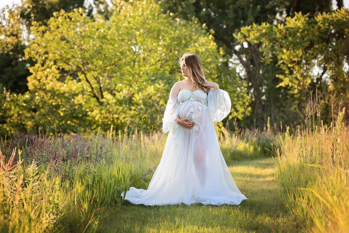 Wearing a beautiful gown, an expectant mother holds her belly during her session.