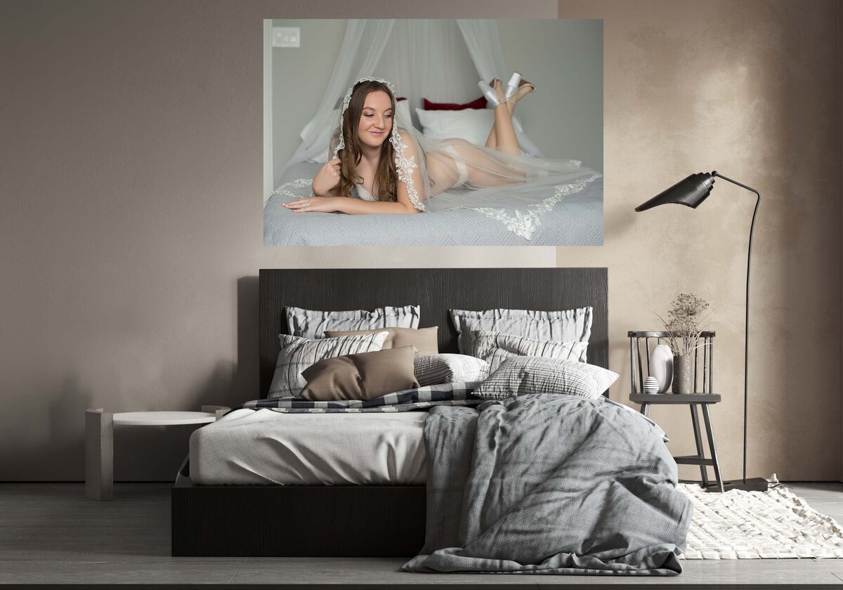 A canva of a bride hanging over the headboard. The pride in the photos is wearing her wedding veil and white lingerie . She is laying on her stomach and looking to the smile with a smirk on her face.