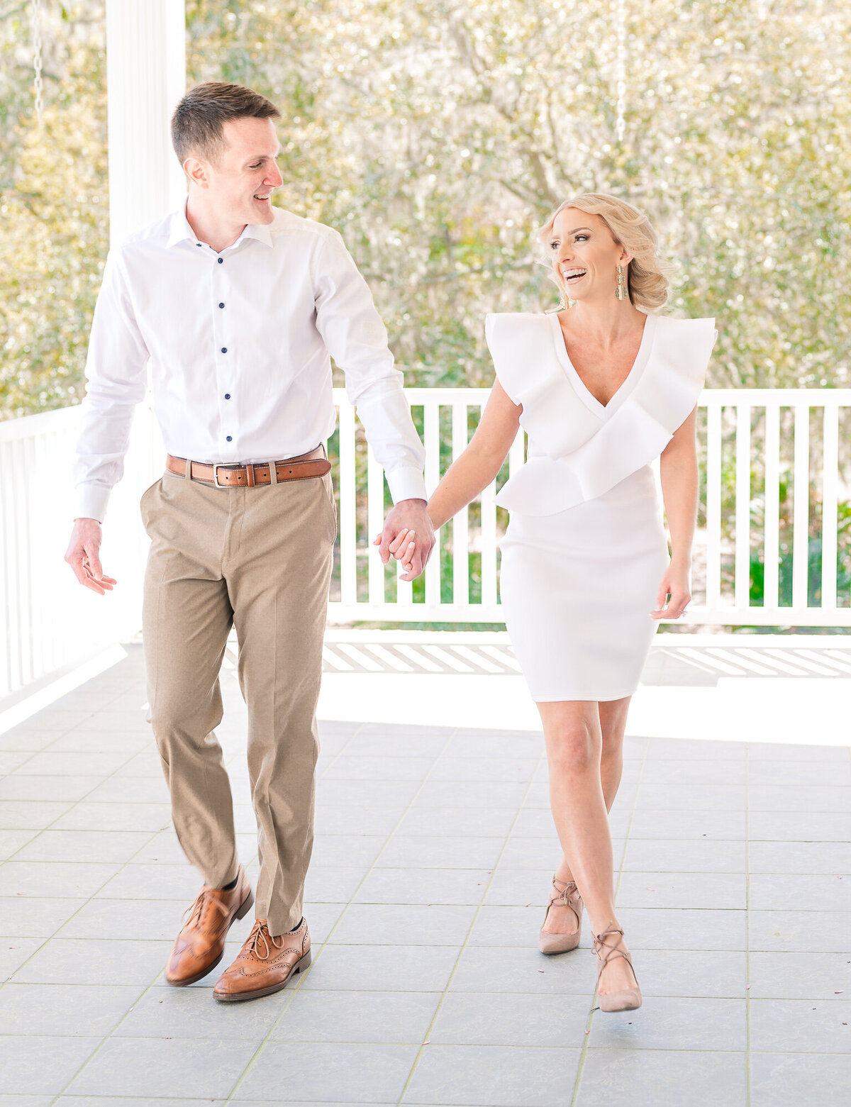A couple walking on a porch of a timeless Raleigh venue for their engagement session by JoLynn Photography, a North Carolina wedding photographer