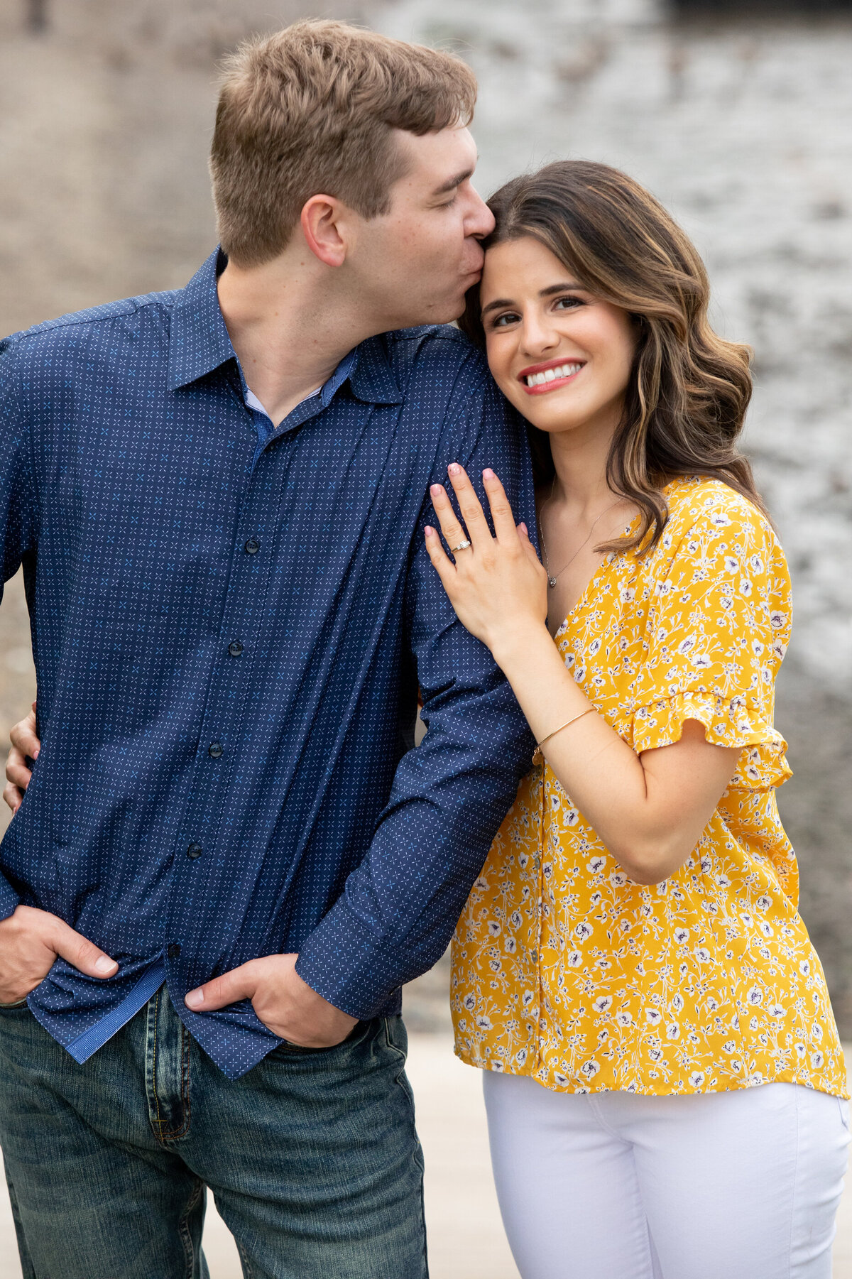 A man in navy shirt kisses a woman dressed in yellow showing offer her diamond ring engagement session New York wedding photographer