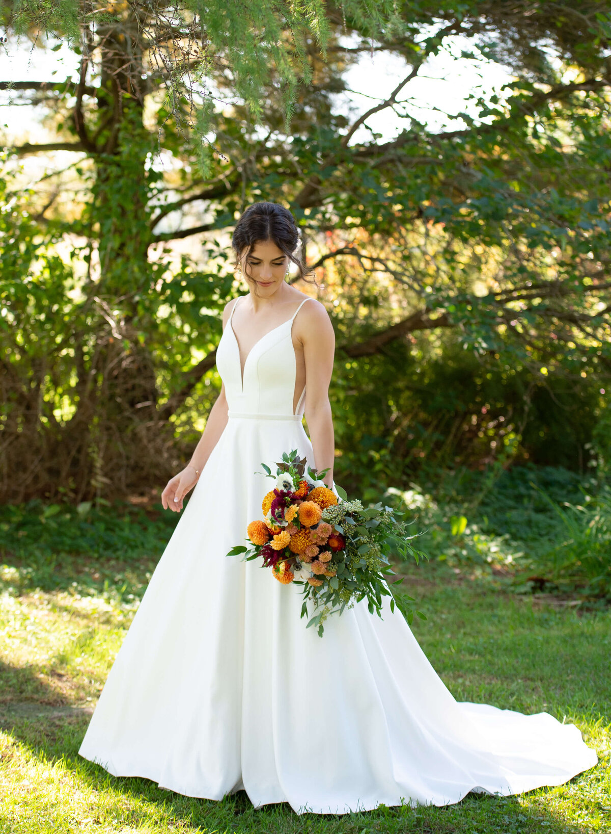 a full length photo of a pretty bride in her simple gown holding a fall coloured orange wedding bouquet for her Strathmere wedding in Ottawa.  Captured by Ottawa wedding photographer JEMMAN Photography